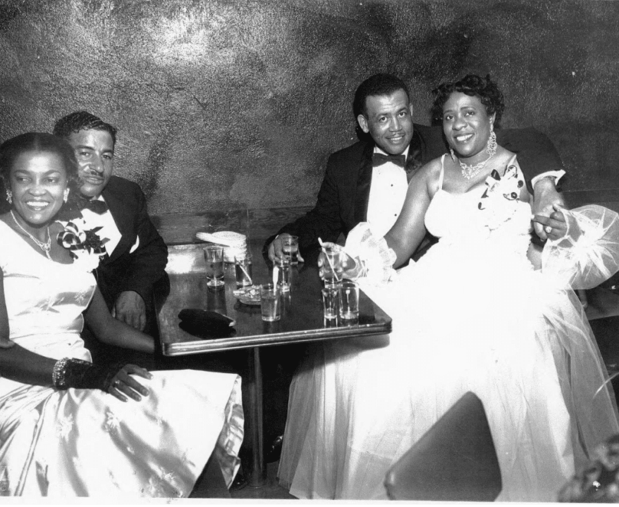 Icon Fannie Mae and friends dressed up at a table with cocktails